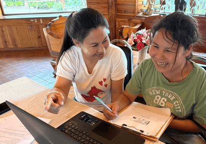 Two women sit at a laptop. 