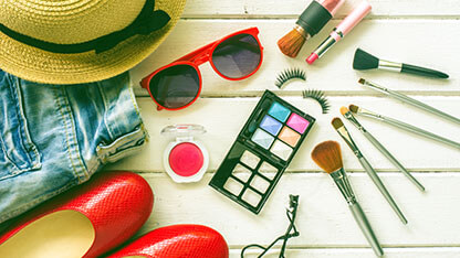 Close-up view of accessories laid out on table including; hat, jeans, shoes, and makeup