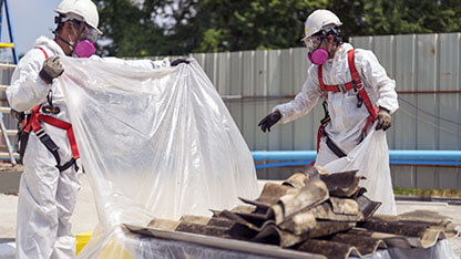 Workers wearing full body protective clothing while working with the asbestos roof tiles. Hazardous waste management and working safety concept. Professional waste disposal.