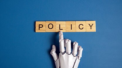 White robotic hand pointing to the word policy on wooden blocks over a blue background representing artificial intelligence ethics and government regulations. 